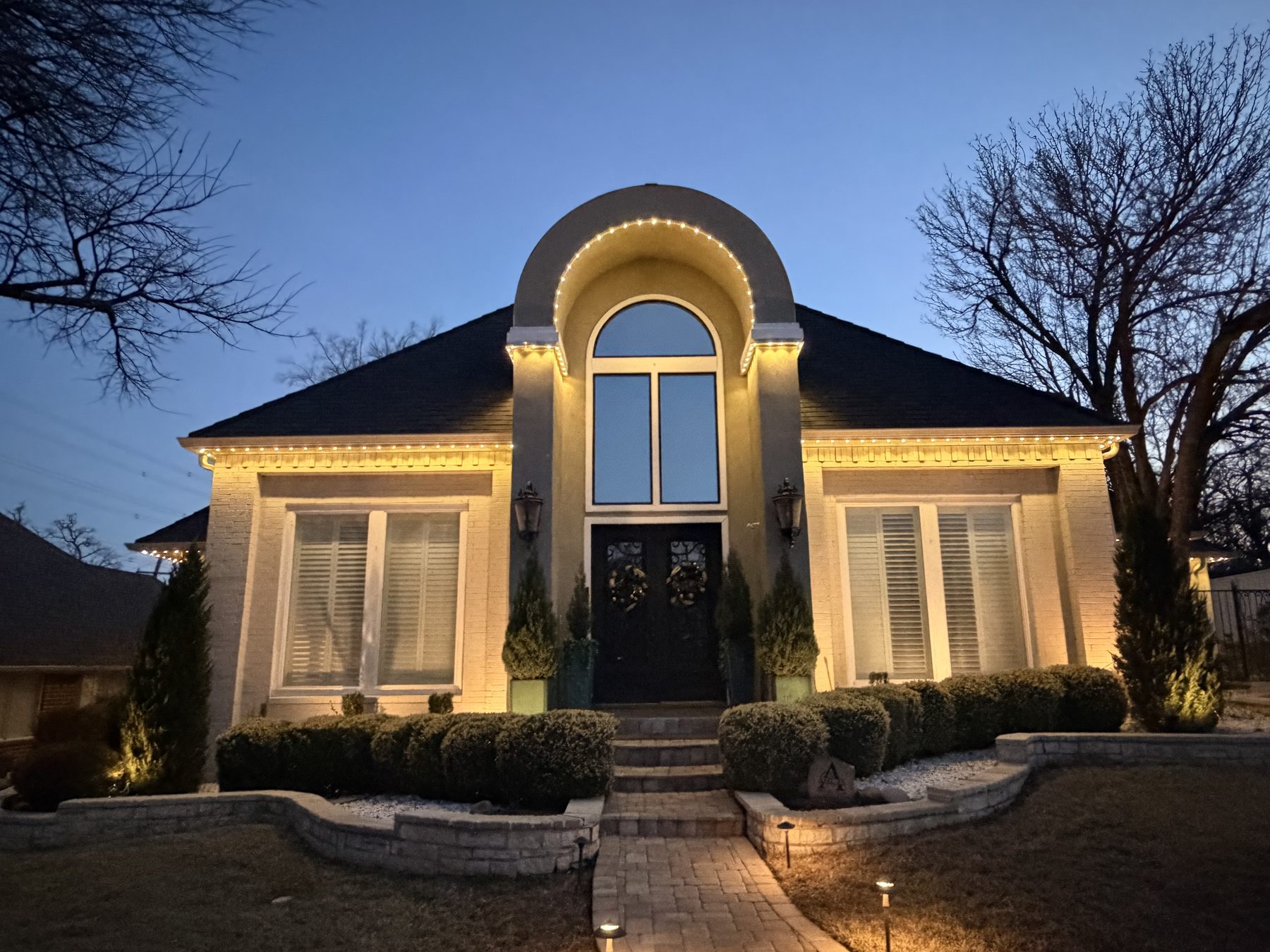 Arched entryway traced in warm white permanent lighting at dusk