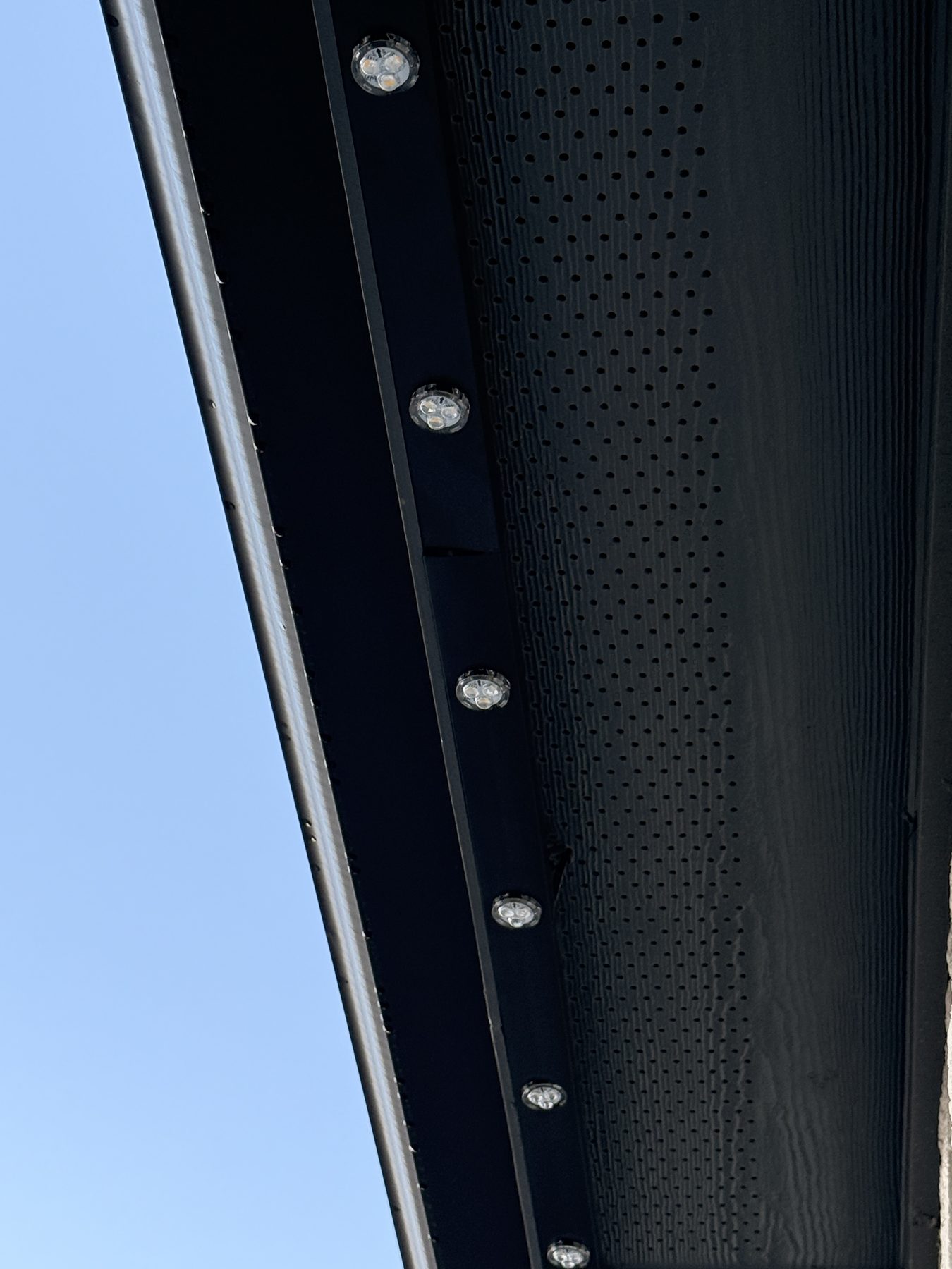 Daytime close-up of black track and LED pucks mounted on a soffit