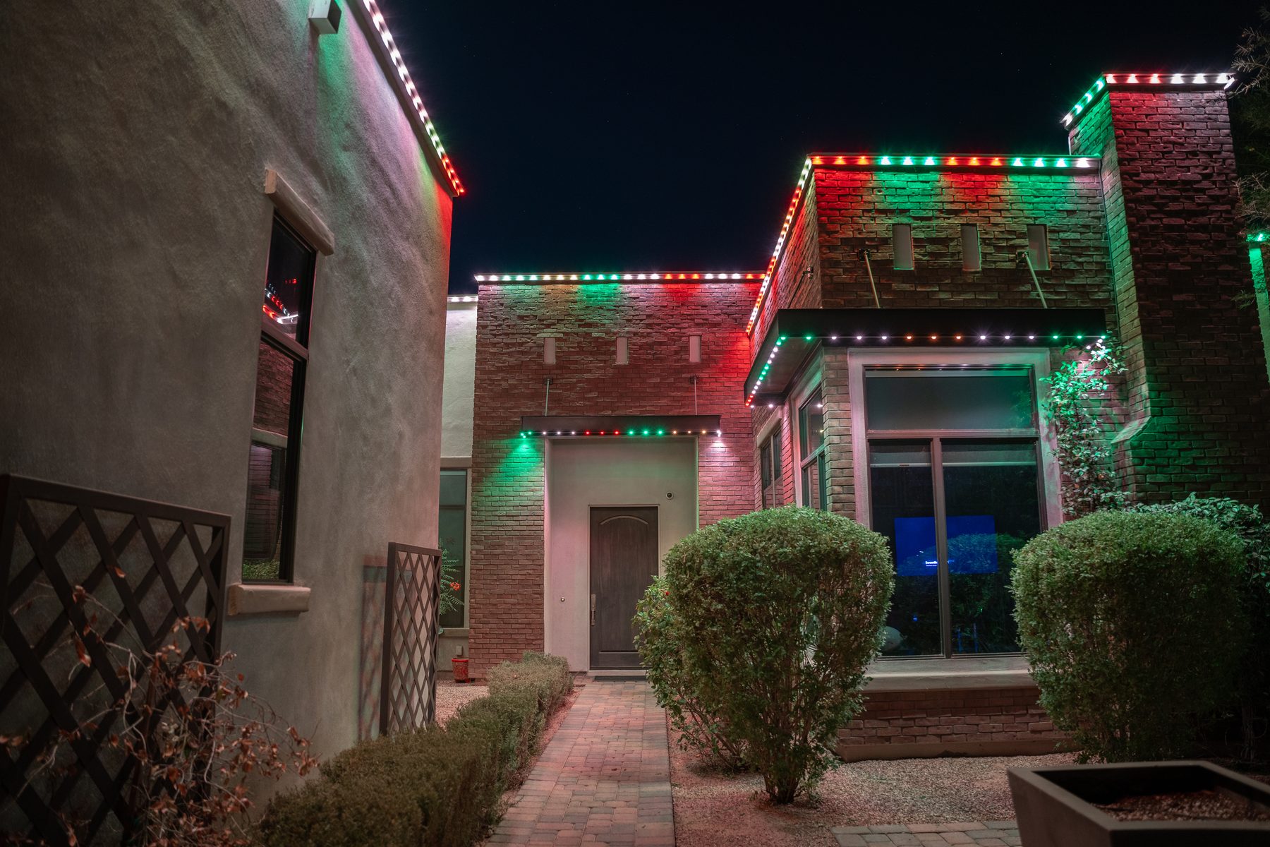Modern stucco and brick courtyard washed in red and green holiday lighting