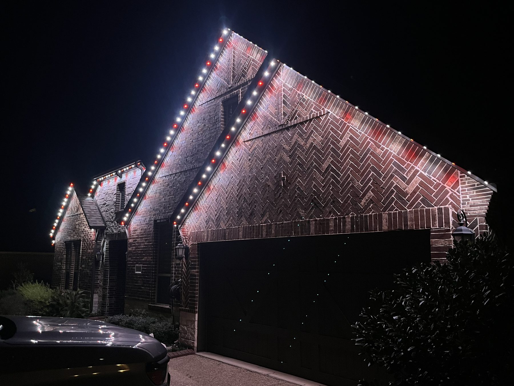 Herringbone brick home lit with alternating red and white holiday lights