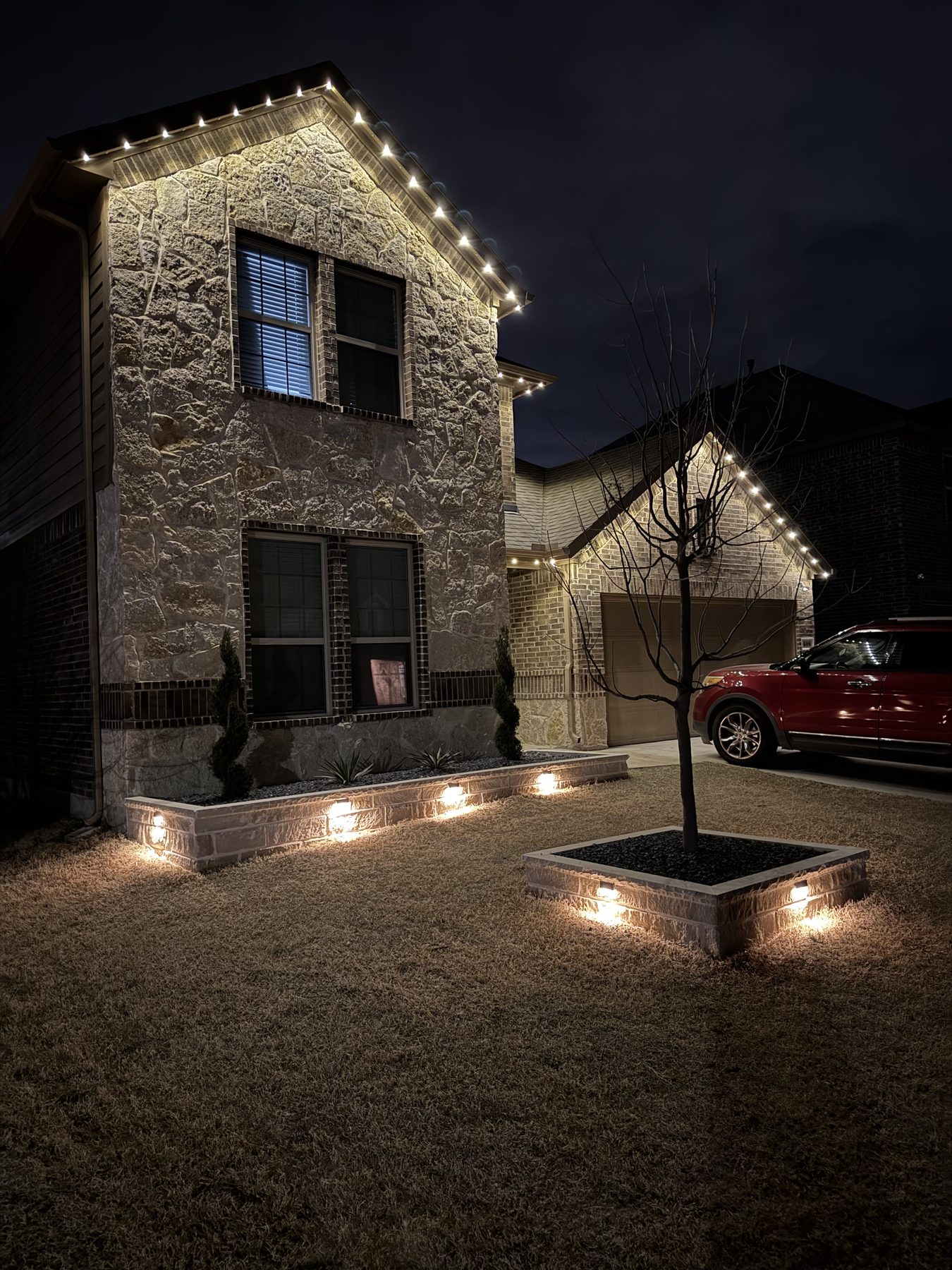 Stone home with lit landscape beds and roofline lighting