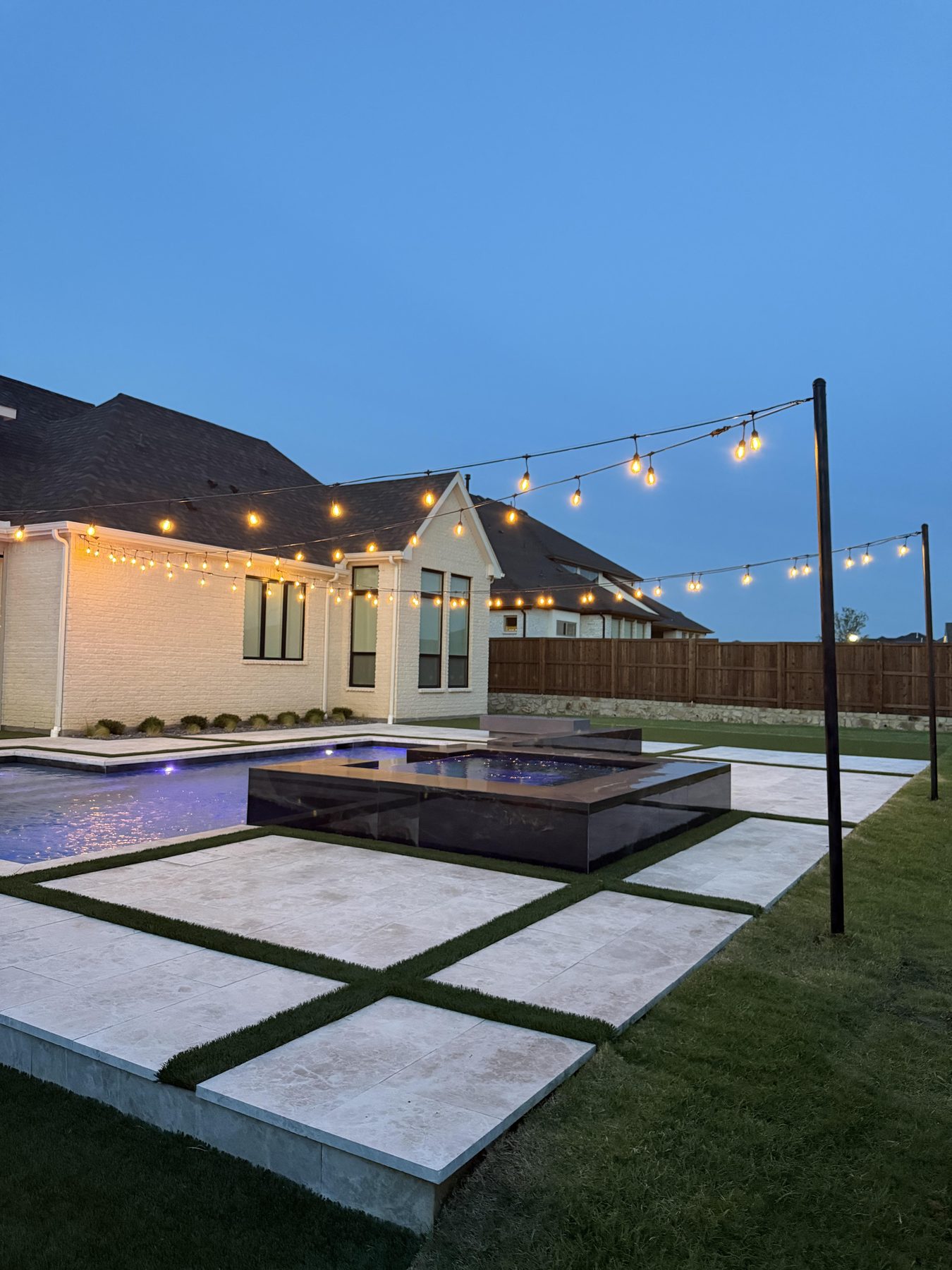 Cafe string lights on poles over a modern pool and spa